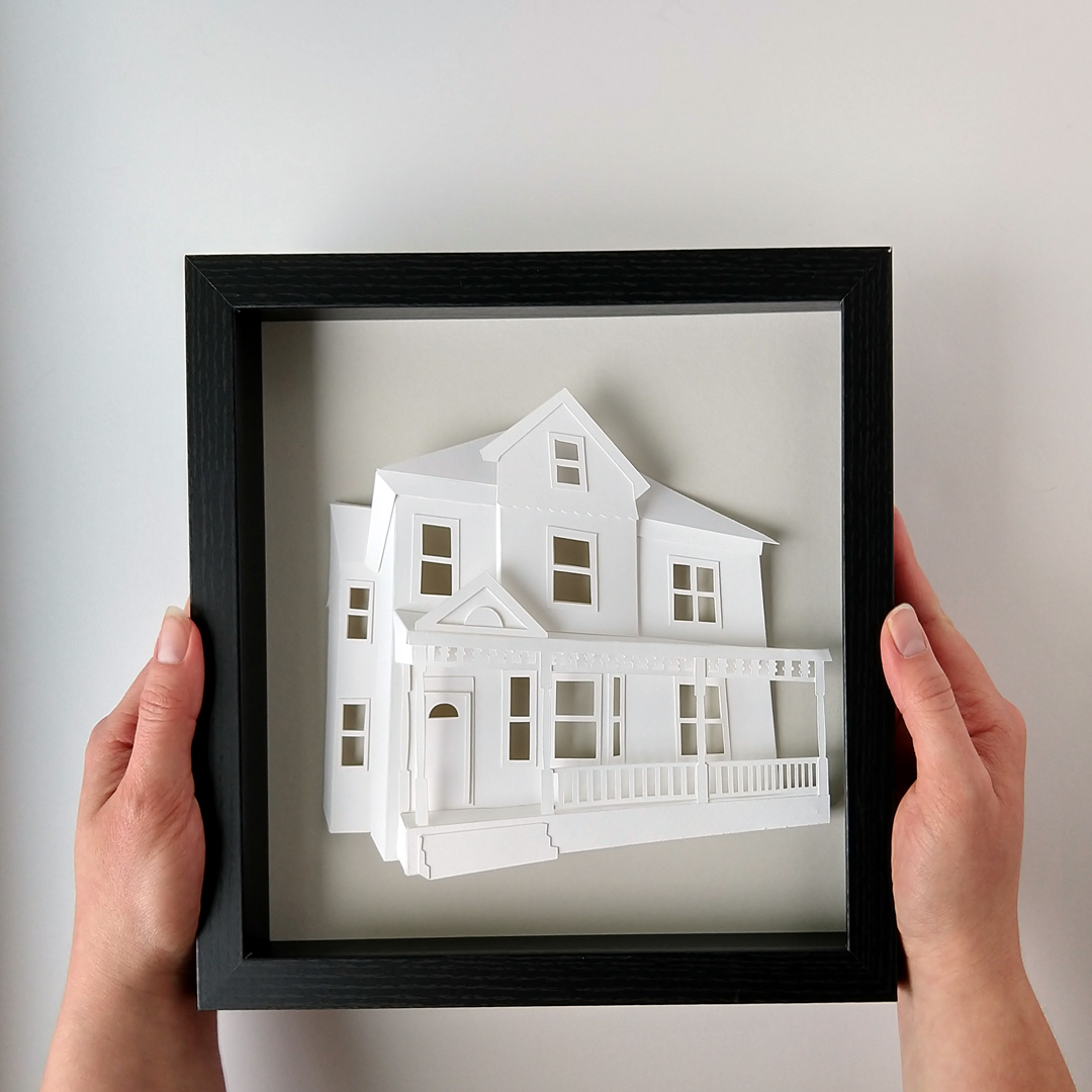 two hands holding a paper model of a house