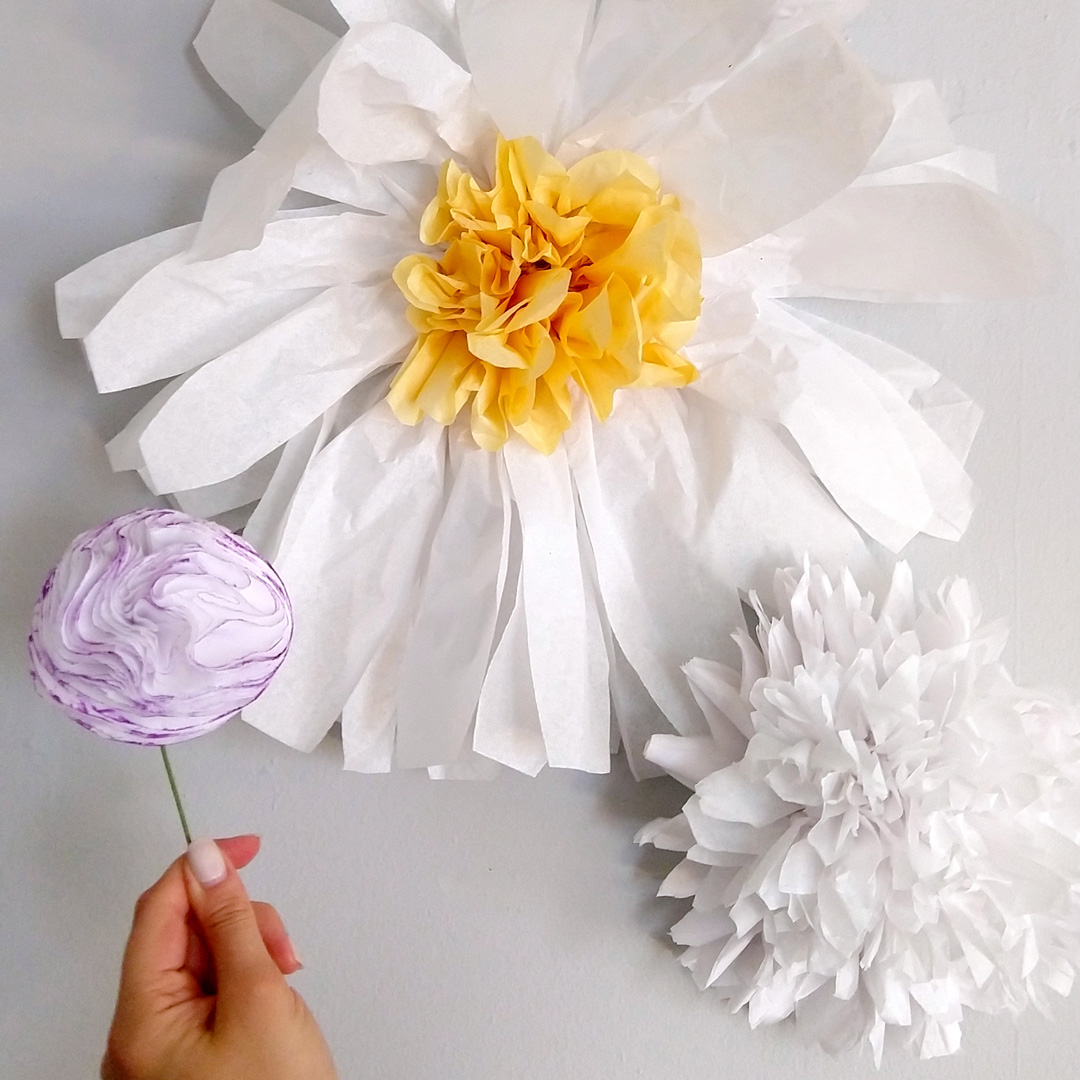 a hand holding a flower next to two paper flowers