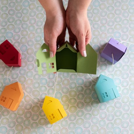 a child's hands holding a paper house on top of a table