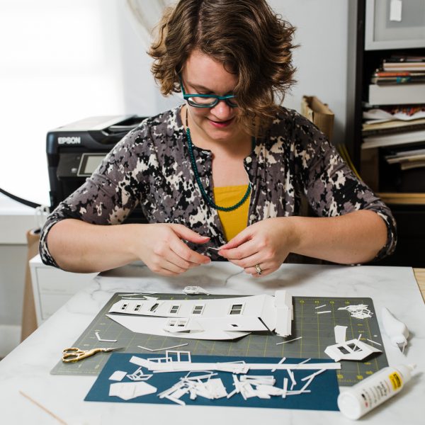 Artist Abigail McMurray assembling a custom paper house portrait in her home studio