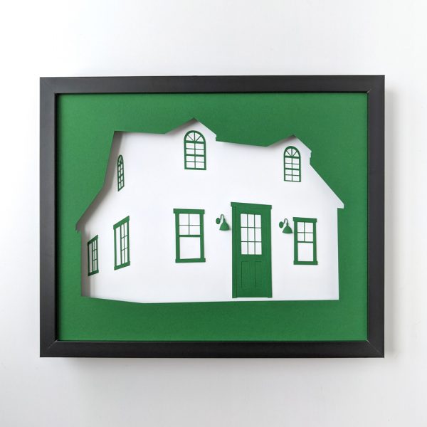 Framed paper art depicting the "Making It" cottage in dark green and white paper
