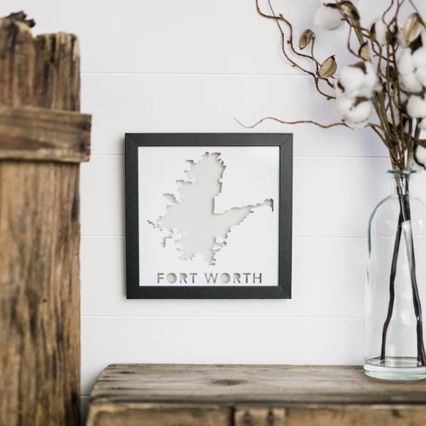 Custom Paper Place showing the city of Fort Worth, TX with a light gray background hanging on a white wall with distressed wood surface below and to the left