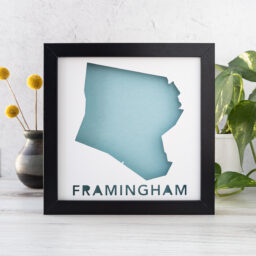 a black frame with the shape of framingham, ma cut from white paper to reveal a light blue background