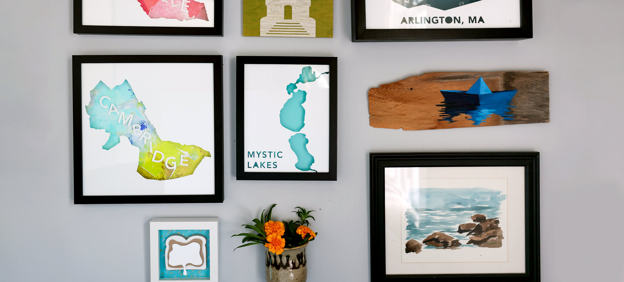 A gray gallery wall featuring Paper Places artworks by Abigail McMurray among other artwork